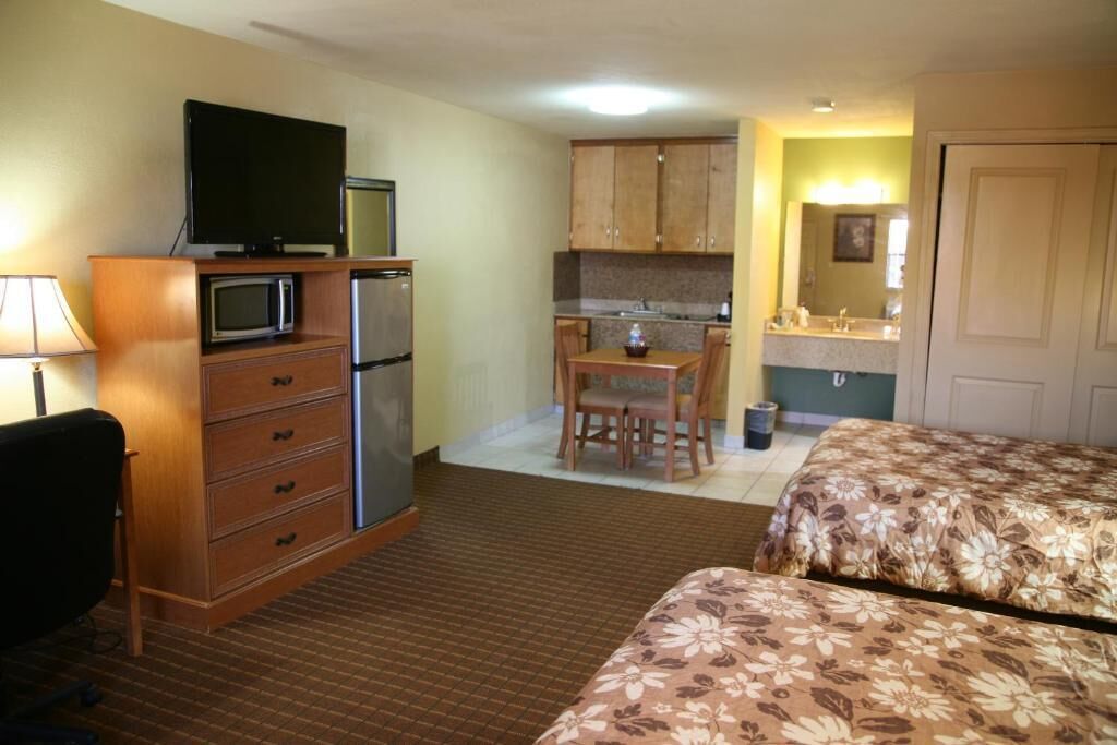 A hotel room with a kitchenette, a TV, a desk, and two beds.