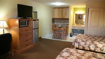 A hotel room with a kitchenette, a TV, a desk, and two beds.