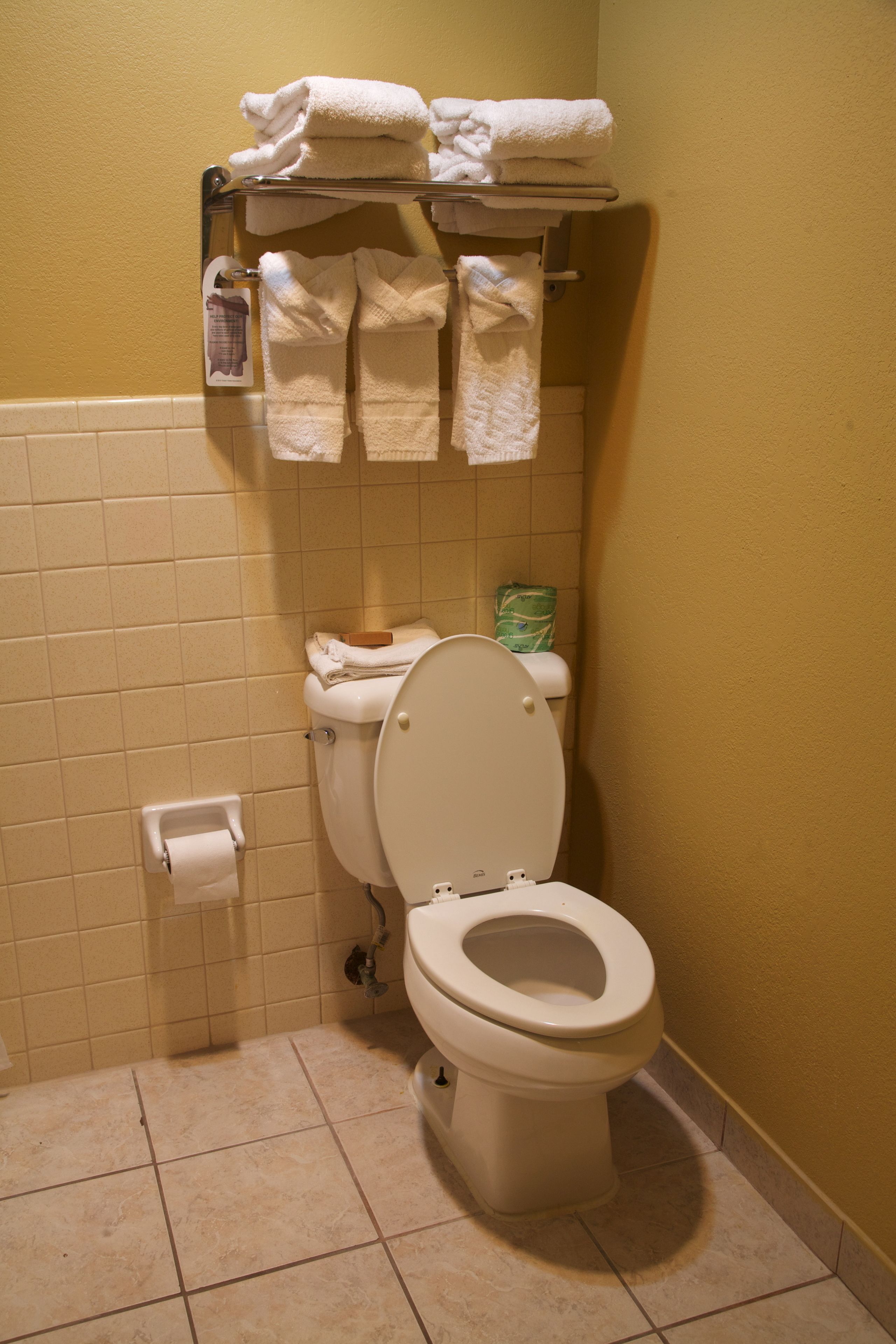 A bathroom with a toilet, a towel rack with folded towels, and a toilet paper holder.