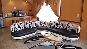 Un salón con un sofá y un juego de butacas estampado en blanco y negro con motivos de vaca, una cafetera y una mesa de comedor.