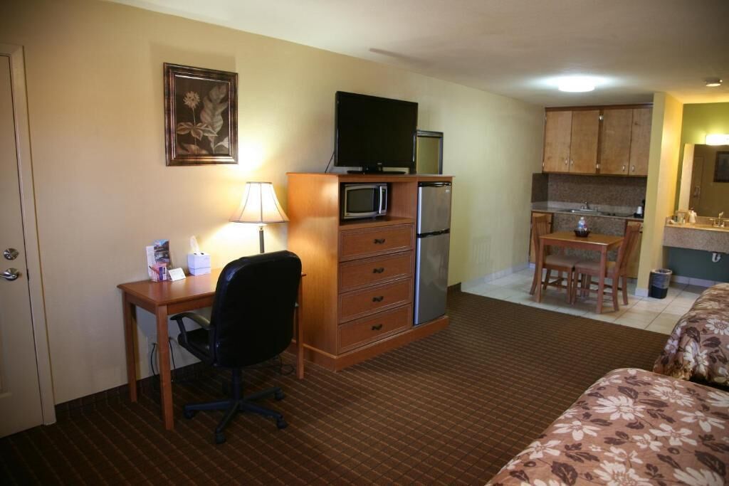 A compact hotel room with a desk, office chair, kitchenette, and a bed.