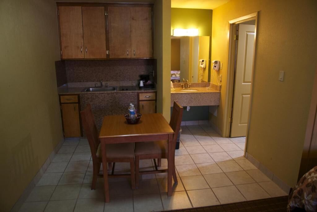 Une cuisine de taille réduite, dotée de meubles de rangement en bois, d’une table à manger avec des chaises et d’un petit plan de travail.