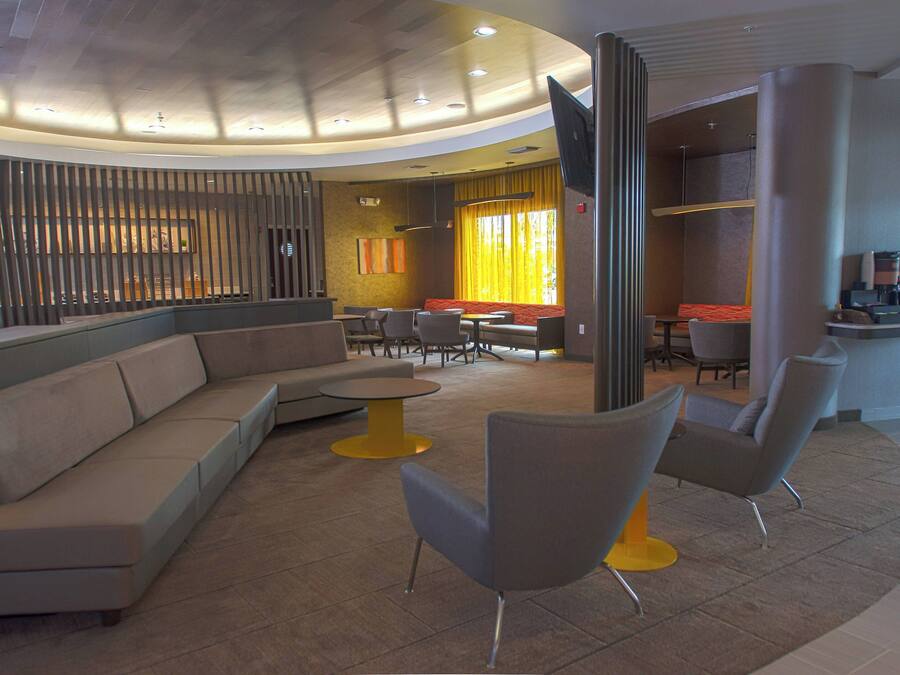 A modern lobby with a curved ceiling, a seating area with sofas and chairs, a coffee bar, and a large window with curtains.
