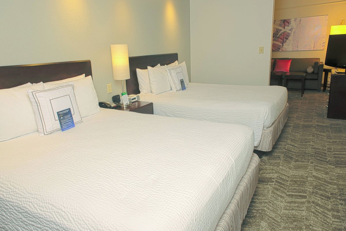 A hotel room with two beds, a nightstand with a lamp, a desk with a computer, and a TV.