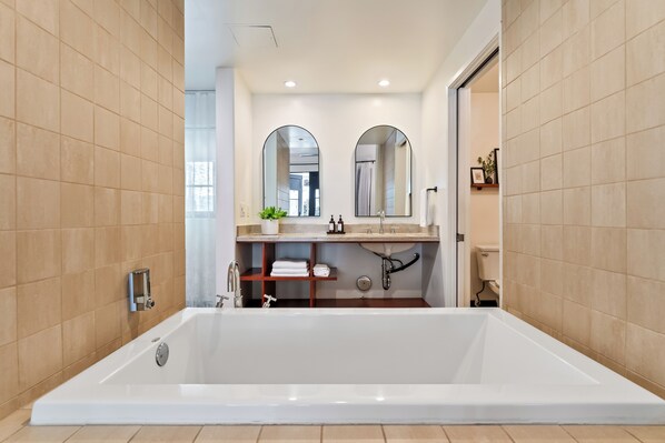 Un baño moderno con una bañera grande, un lavamanos con espejo y un inodoro.
