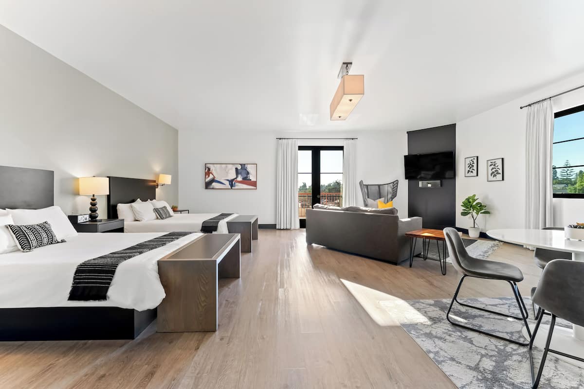 Habitación de hotel moderna con una cama grande, un sofá, un comedor y vistas al exterior.