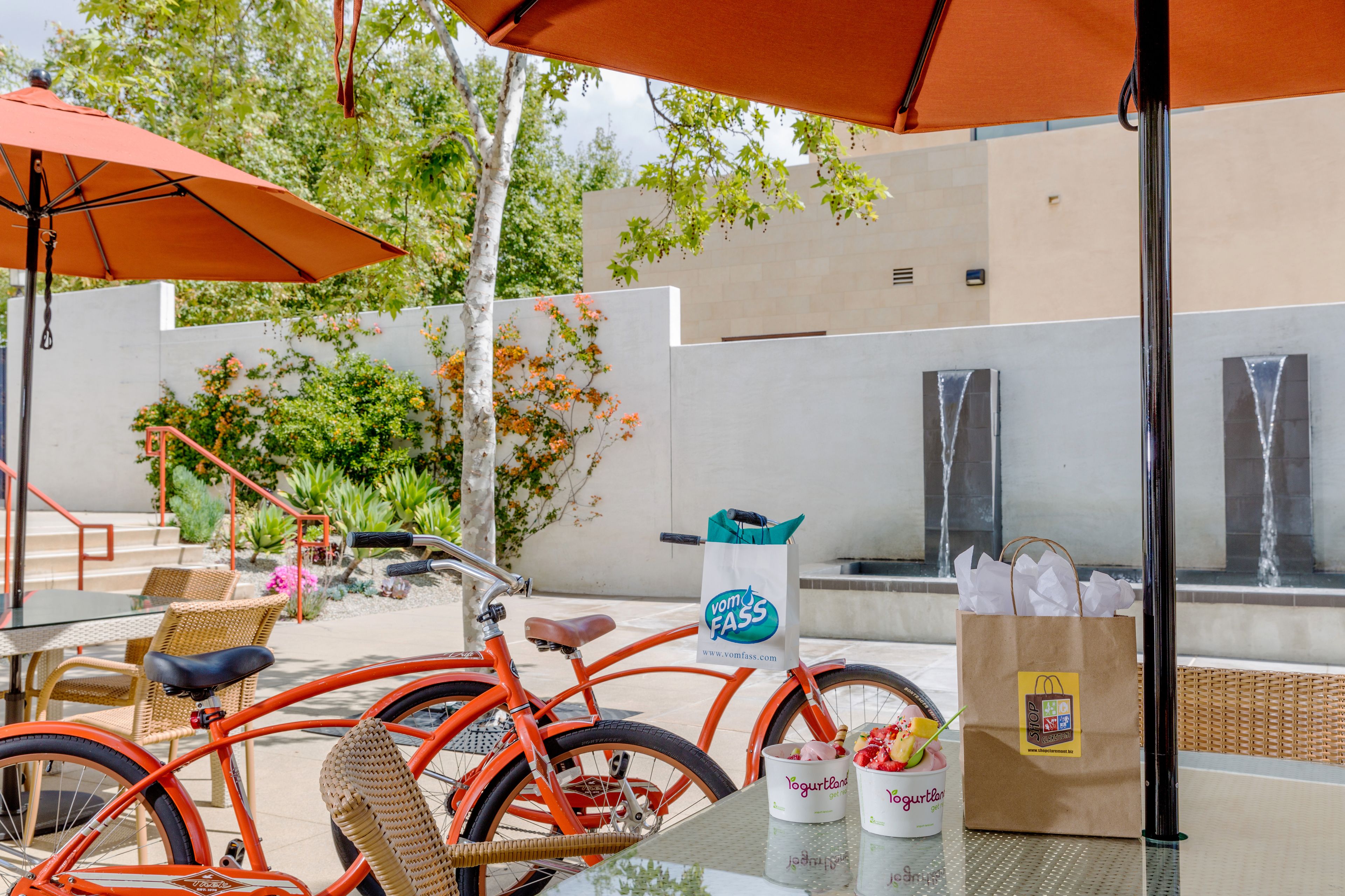 Un espacio al aire libre con una bicicleta, una mesa, sillas y un paraguas grande color naranja.