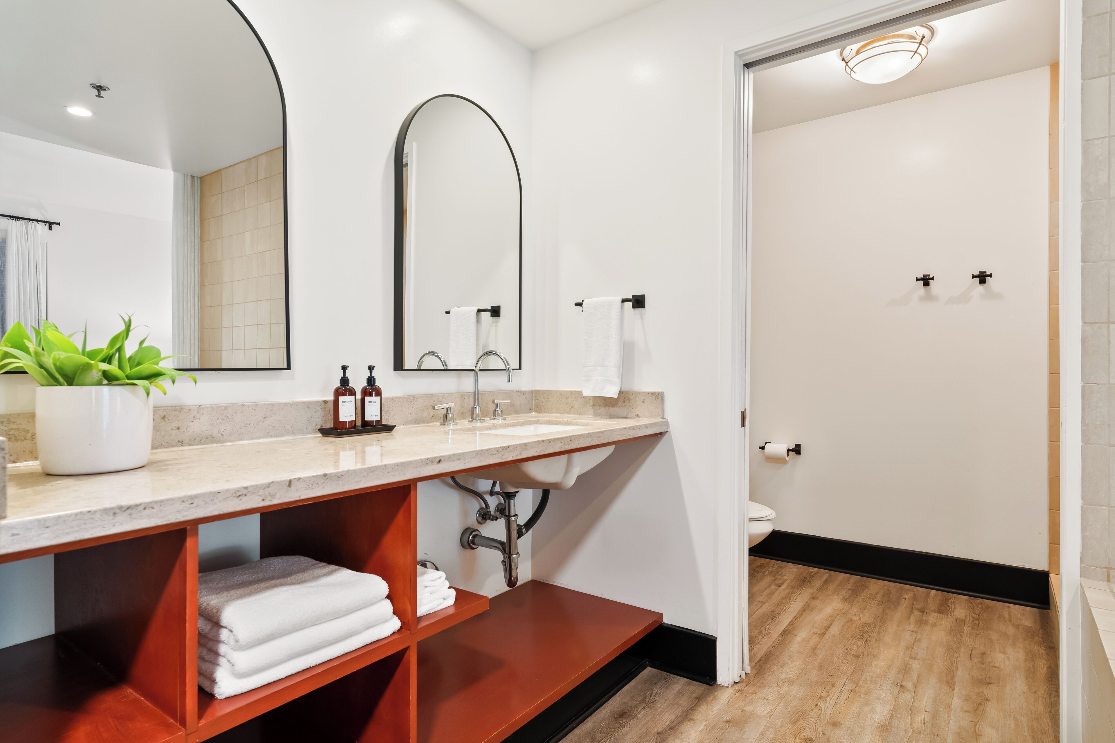 A modern bathroom with a large mirror, a sink, a shower, and a potted plant.