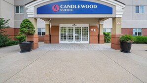 Eingang zum Candlewood Suites mit blauem Schild, Doppeltüren und Blumentöpfen.