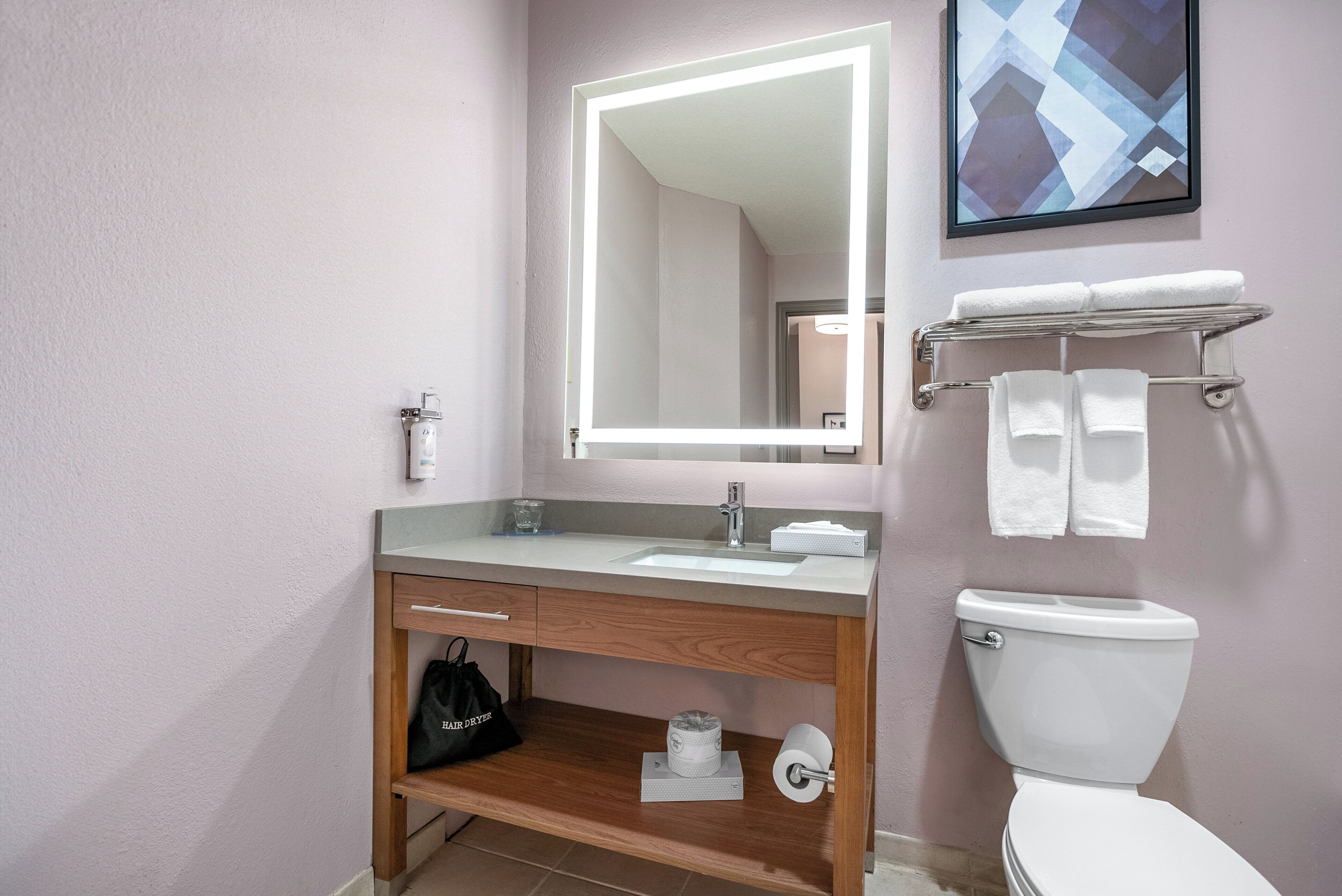 A bathroom with a vanity, sink, mirror, and toilet.