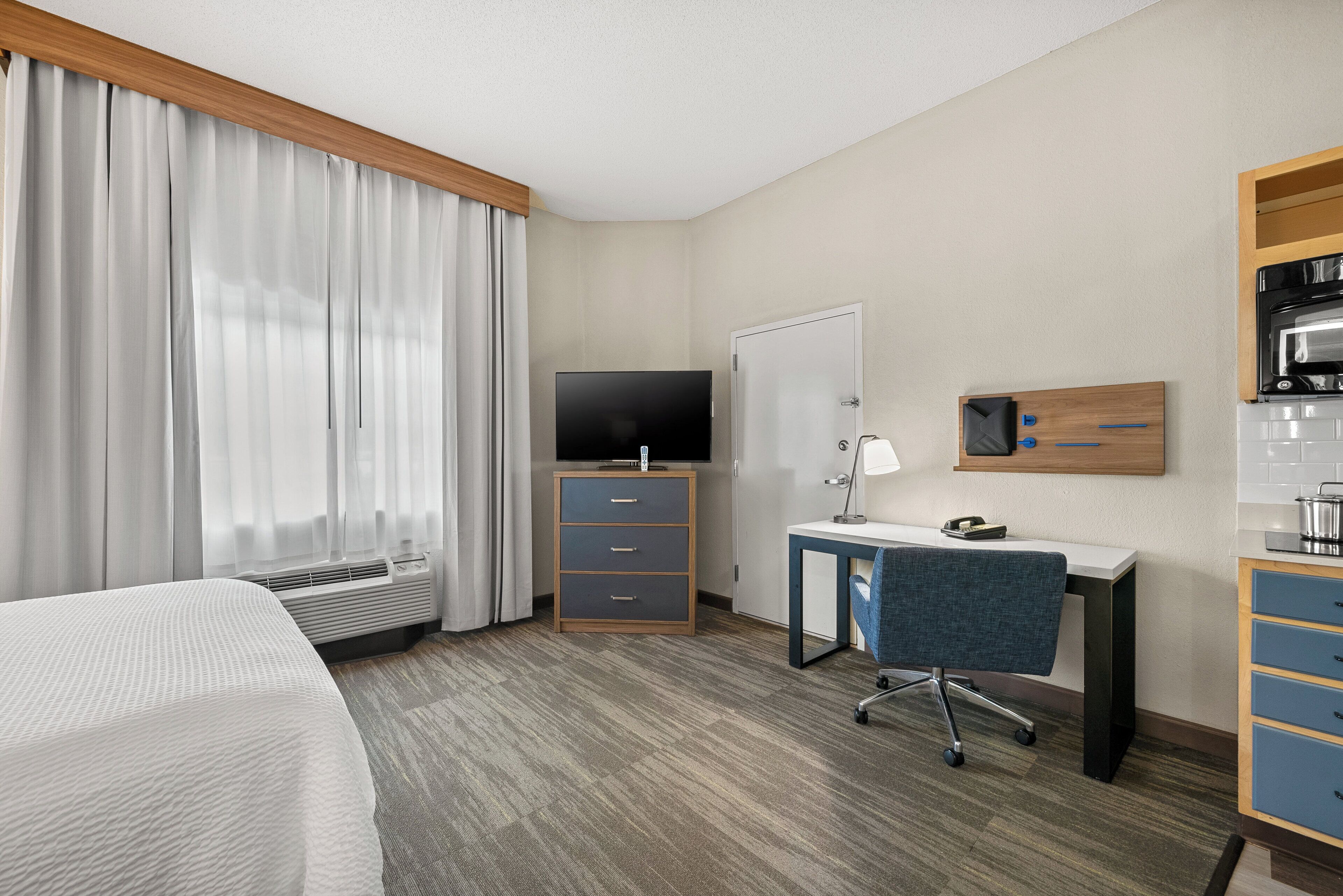 Habitación de hotel con cama, escritorio con silla, televisor, armario y kitchenette.