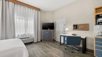 Habitación de hotel con cama, escritorio con silla, televisor, armario y kitchenette.