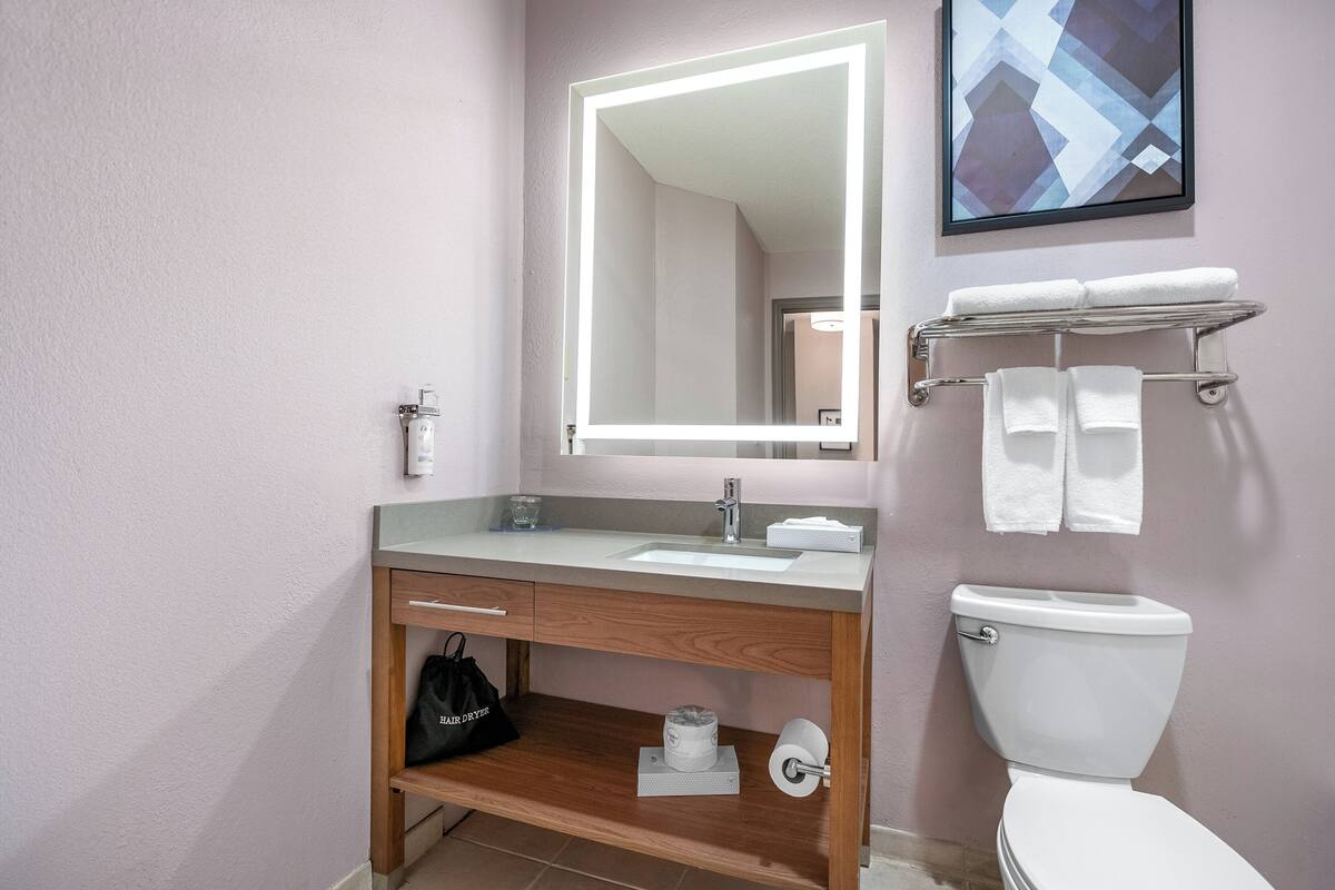 A bathroom with a vanity, sink, mirror, and toilet.