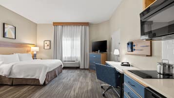 Ett hotellrum med en säng, ett skrivbord, ett litet kök, en TV och ett fönster med gardiner.