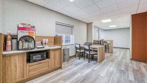 A kitchenette area with a coffee machine, microwave, and storage cabinets. There is a window with blinds and a table with chairs. - Candlewood Suites Bordentown-Trenton by IHG (Bordentown)