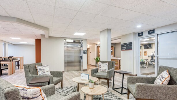 A modern lobby with grey upholstered sofas, a coffee table, a reception desk, and a visible elevator. - Candlewood Suites Bordentown-Trenton by IHG (Bordentown)