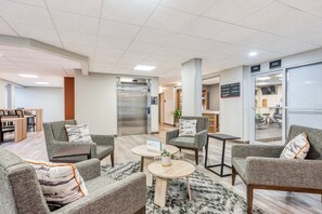 A modern lobby with grey upholstered sofas, a coffee table, a reception desk, and a visible elevator. - Candlewood Suites Bordentown-Trenton by IHG (Bordentown)