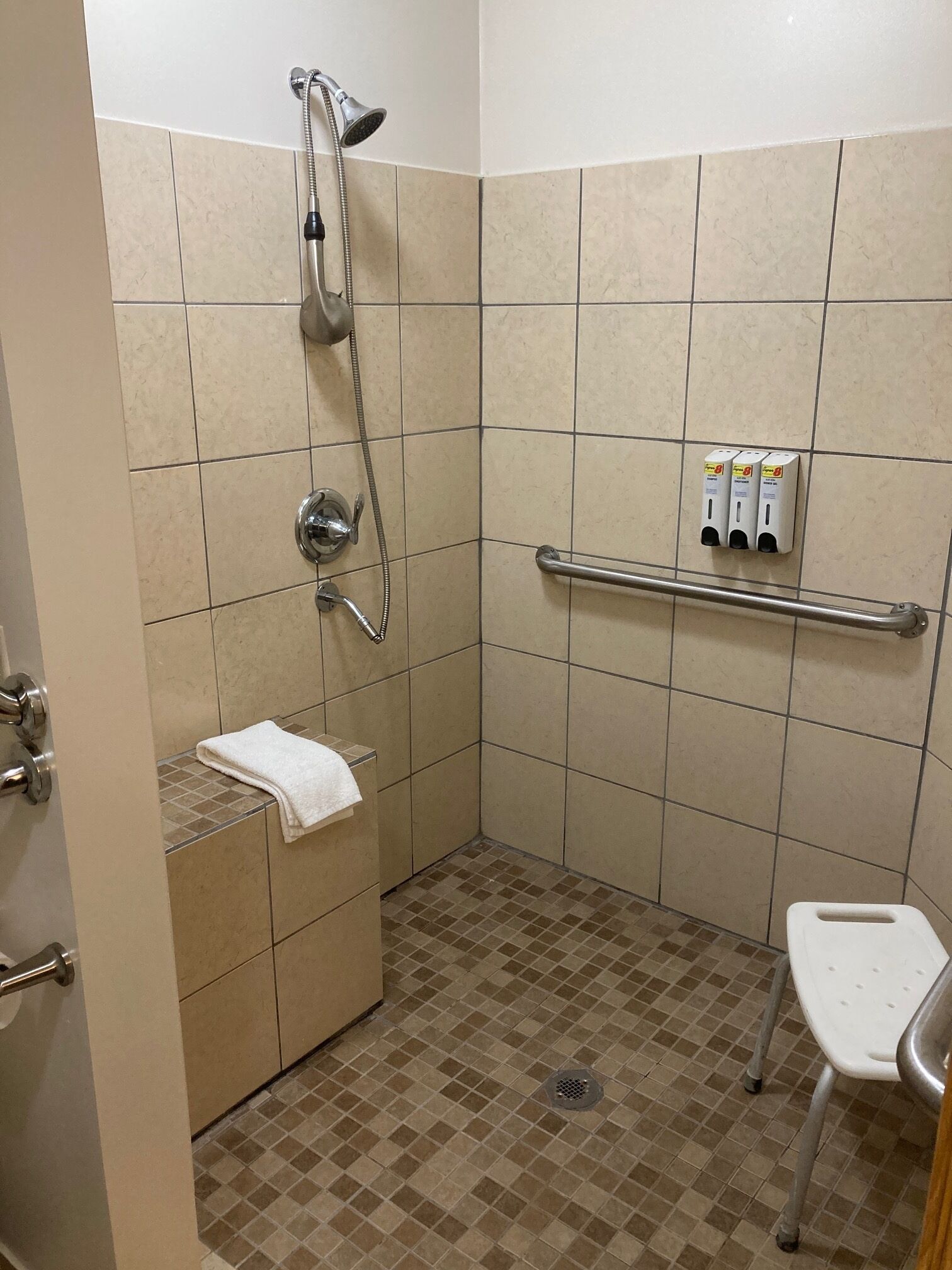 A small, tiled bathroom with a shower, a hand dryer, and a grab bar.