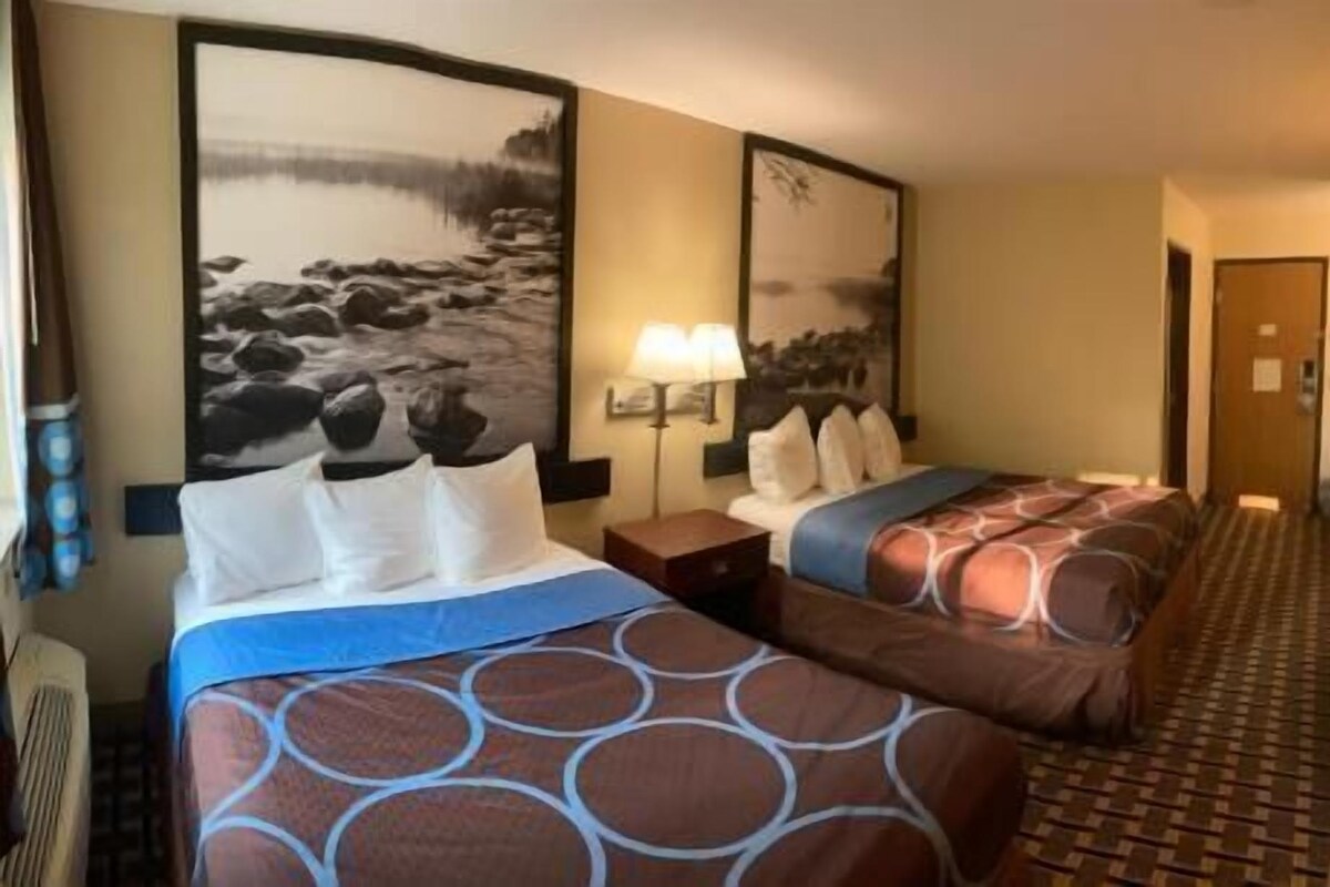 A hotel room with two beds, a large wall painting, a nightstand, and a patterned carpet.