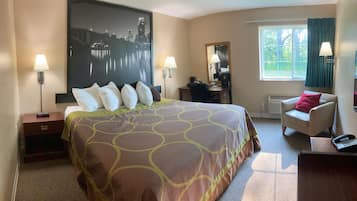 Een hotelkamer met een groot bed, twee bedlampjes, een bureau met stoel, een raam met gordijnen en een spiegel aan de muur.