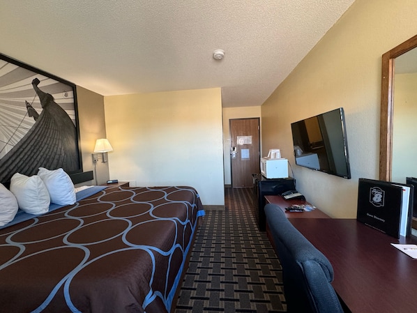 A hotel room with a bed, a desk, a chair, a desk lamp, a television, and a guest directory.