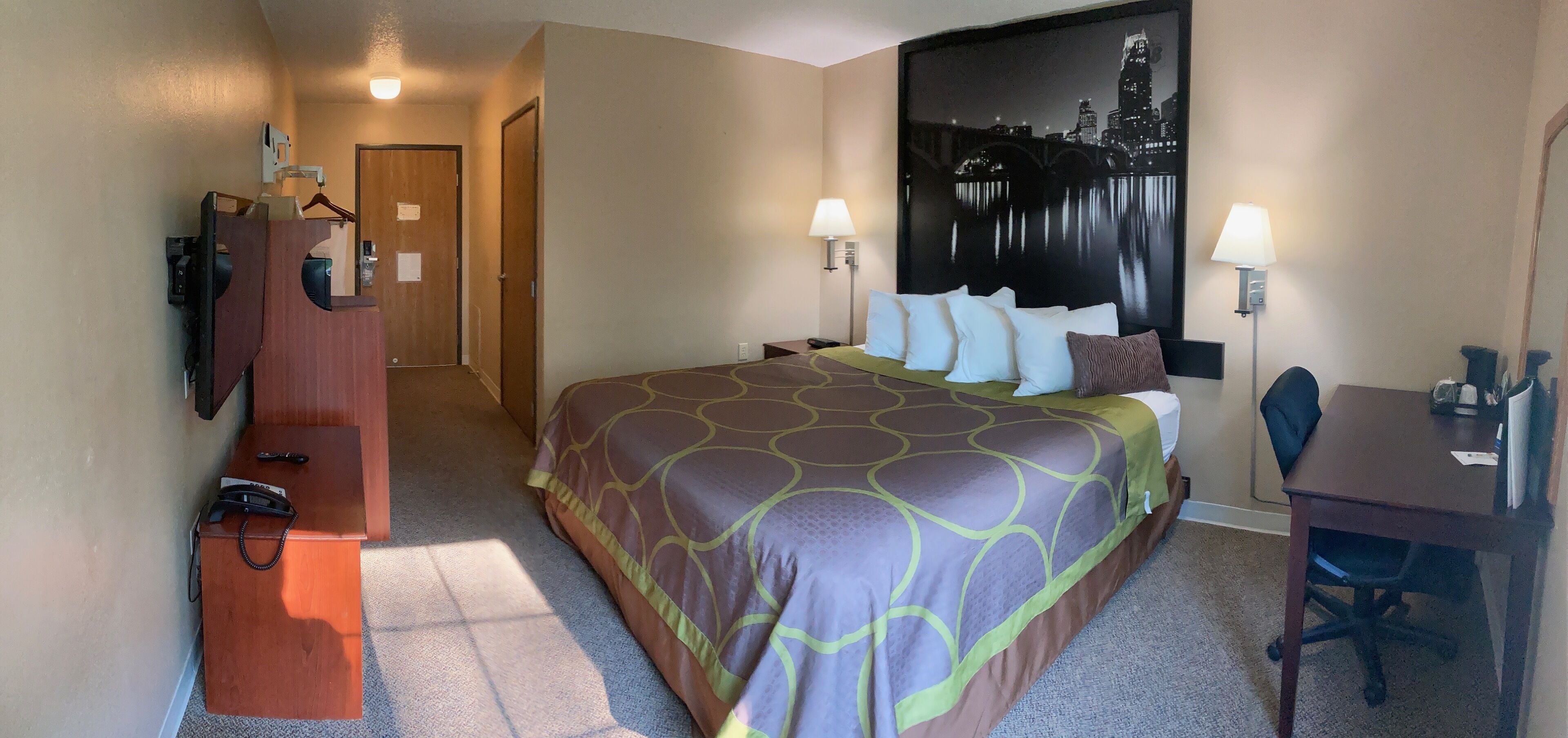 Une chambre d’hôtel avec un grand lit, un bureau, une chaise, une lampe de bureau, un téléphone et un téléviseur fixé au mur.
