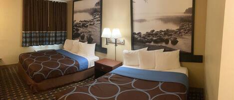 A hotel room with two beds, a nightstand, a lamp, and two large landscape paintings on the walls.