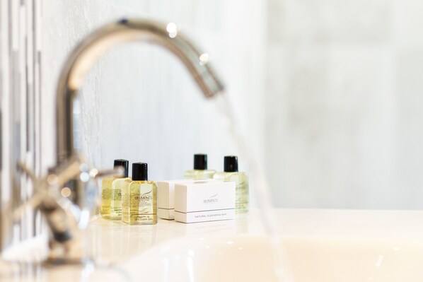 A bathroom with a sink, a mirror, and a faucet. There are three bottles of liquid and a box labeled "Elements Natural Cleansing Bar" on the sink. - Lord Haldon Country Hotel, Sure Hotel Collection by Best Western (Exeter)