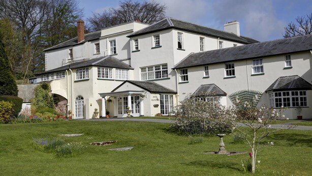 A large, white building with multiple windows and a central entrance, surrounded by a well-maintained lawn and flowering plants. - Lord Haldon Country Hotel, Sure Hotel Collection by Best Western (Exeter)