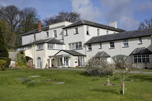 A large, white building with multiple windows and a central entrance, surrounded by a well-maintained lawn and flowering plants. - Lord Haldon Country Hotel, Sure Hotel Collection by Best Western (Exeter)