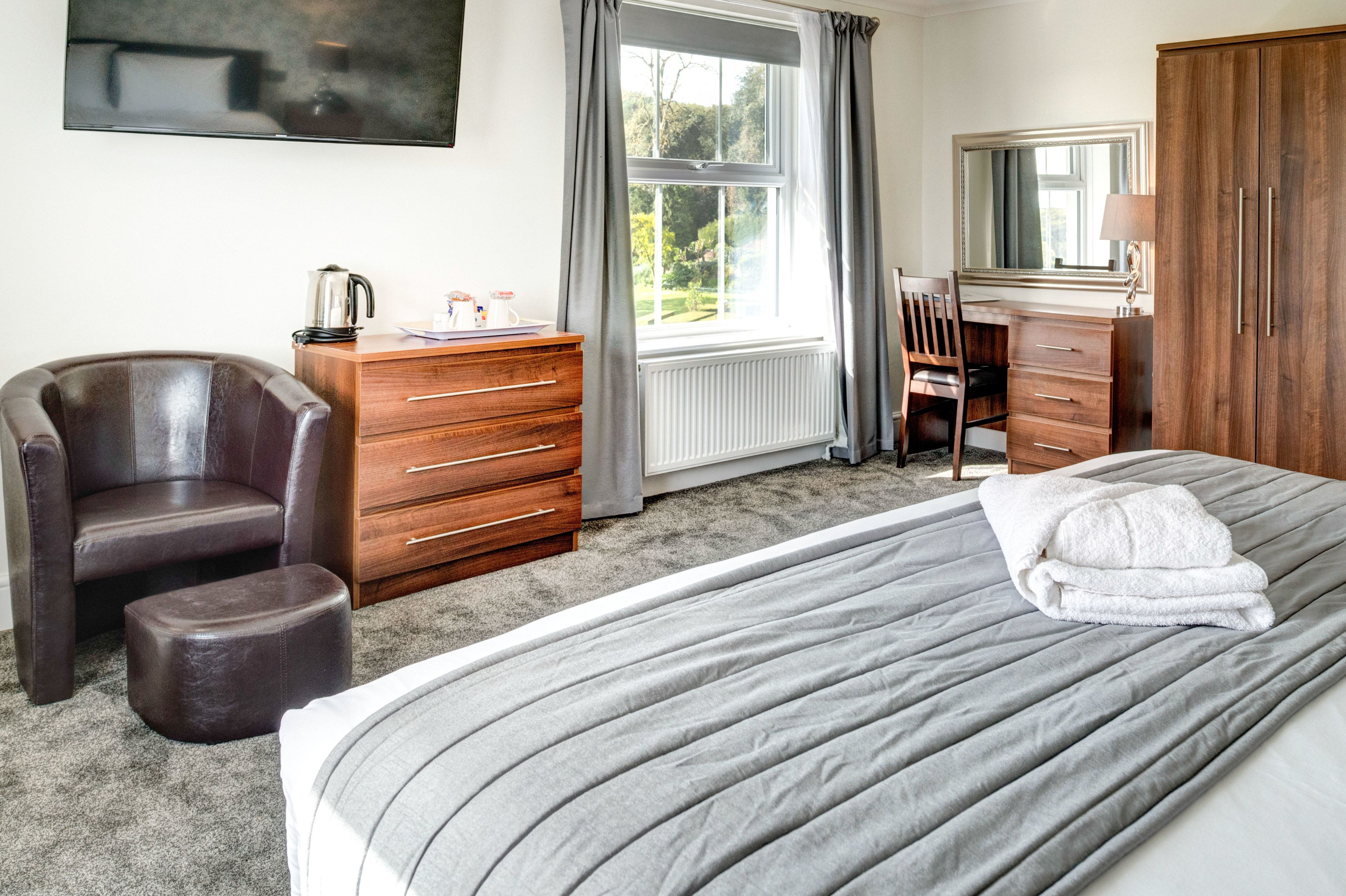 A bedroom with a large bed, a wooden dresser, a leather chair, and a desk with a chair.