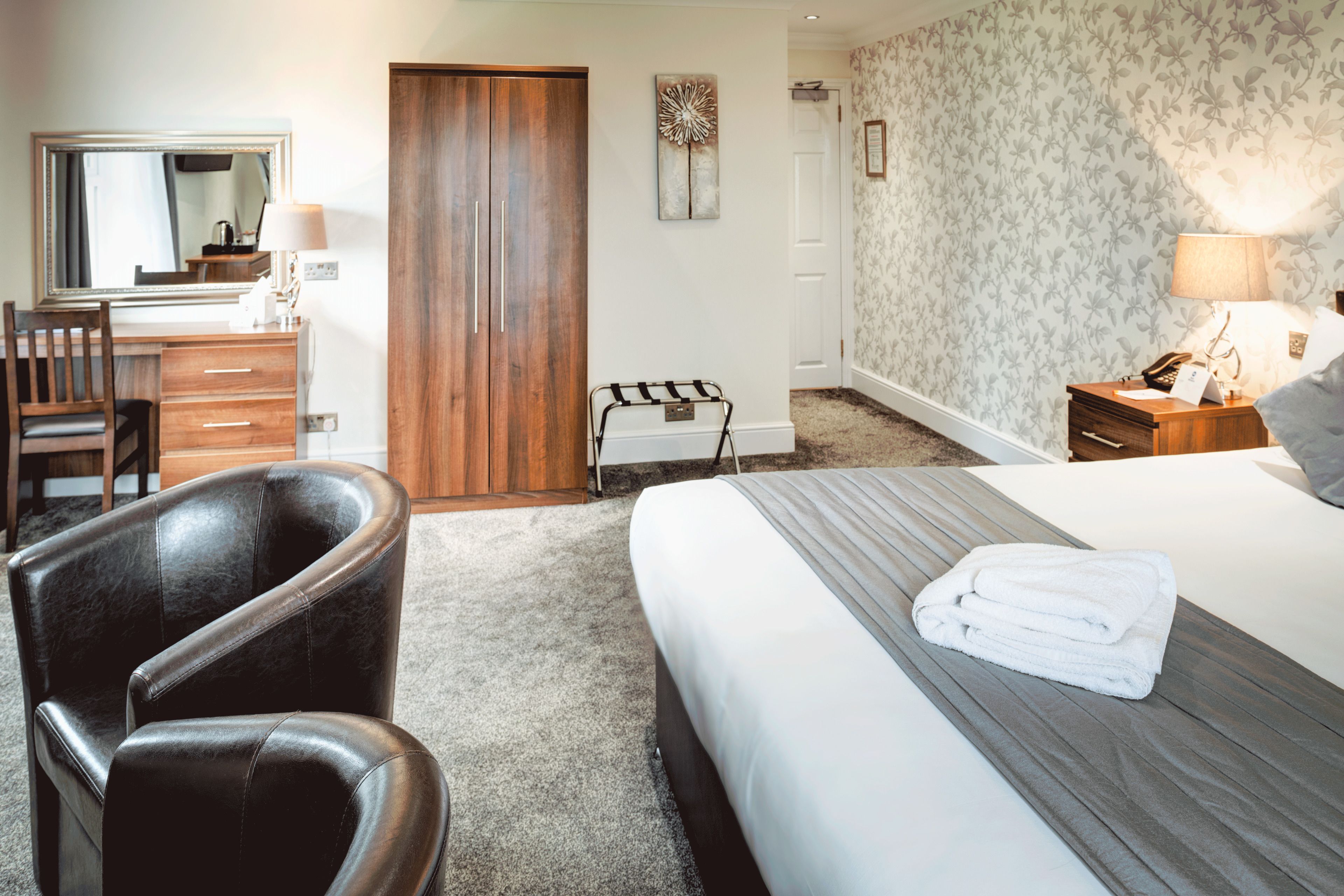 Quarto de hotel com cama, poltrona, secretária, guarda-roupa e banheiro.