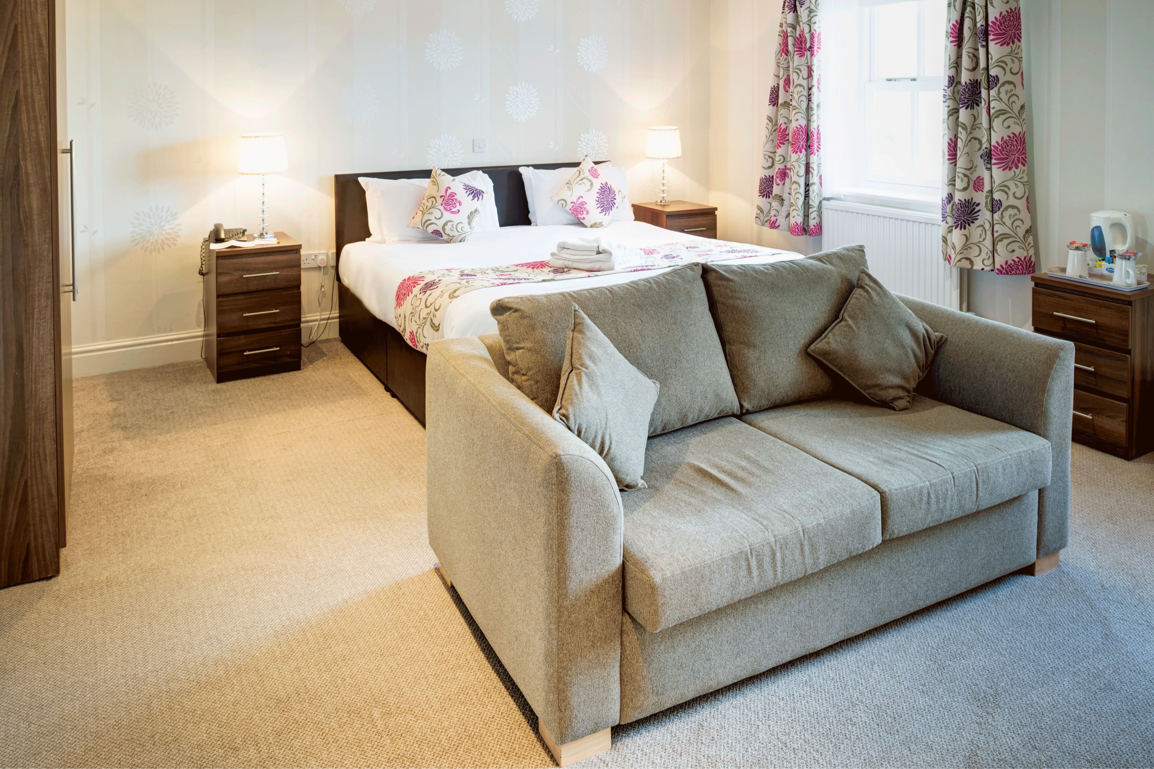 A bedroom with a bed, a sofa, two bedside tables, and a window with curtains.