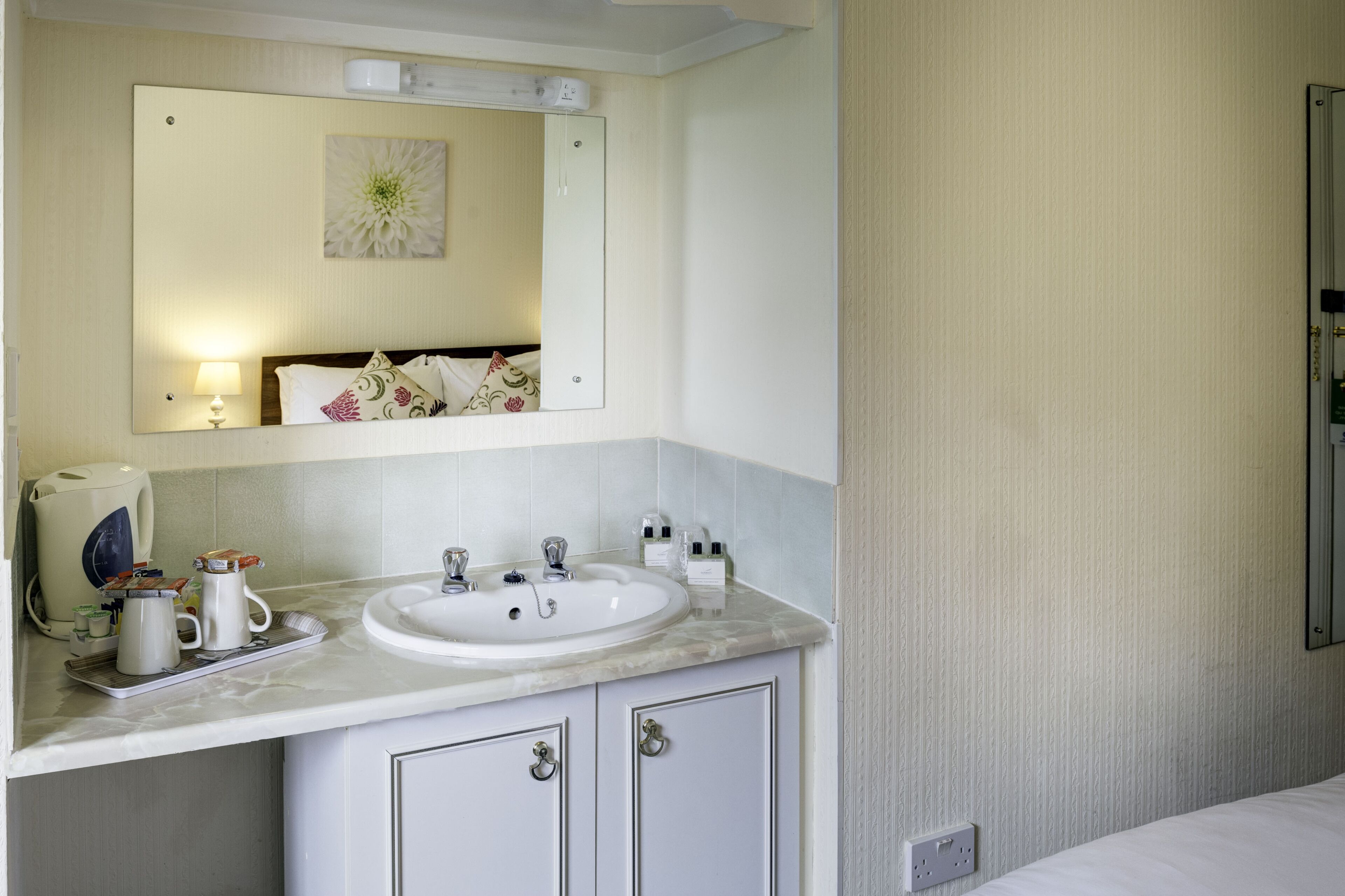 Un bagno con un lavandino bianco, uno specchio e un armadietto. Sopra il lavandino c'è un portasciugamani e un piccolo specchio a parete.
