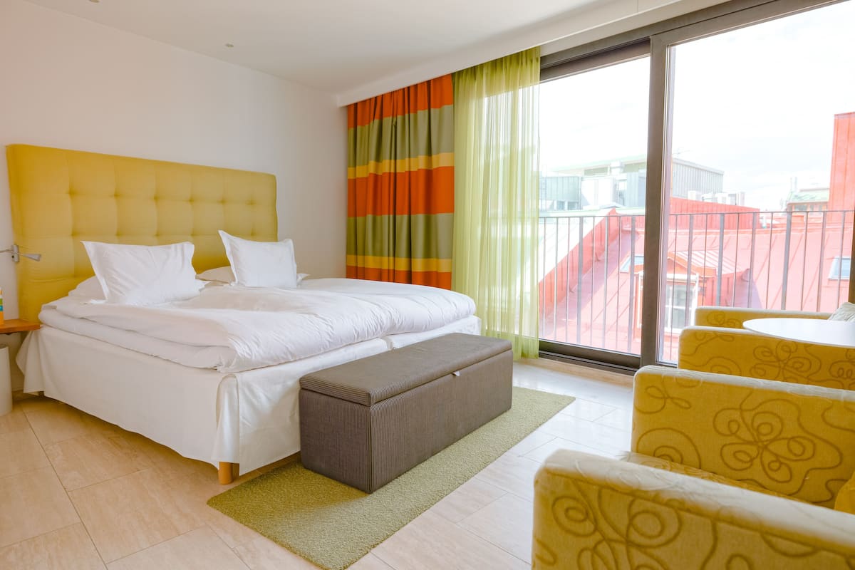 Ett hotellrum med en stor säng, en bänk och gula stolar.
