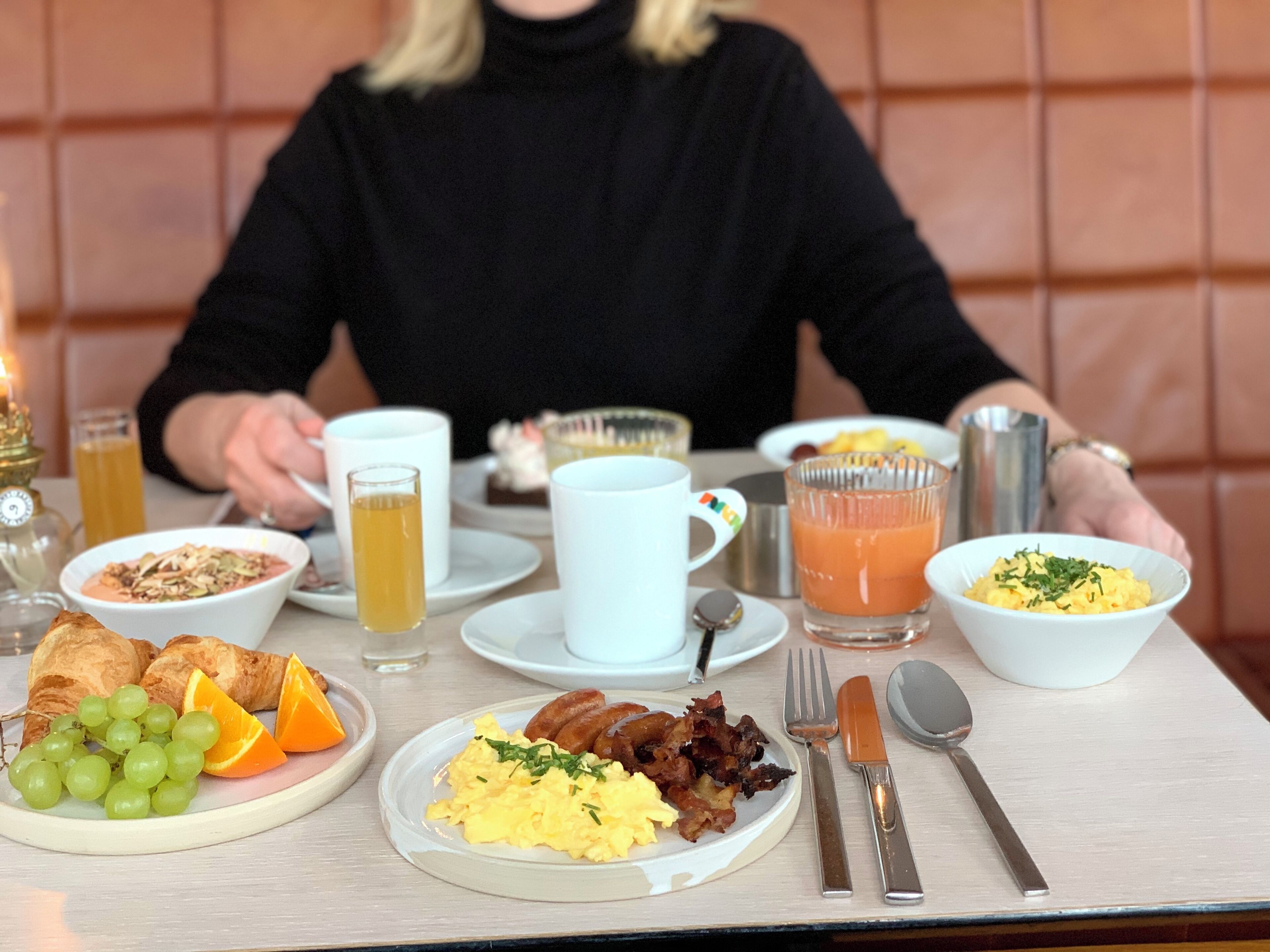 A breakfast table with croissants, eggs, bacon, and fruit.