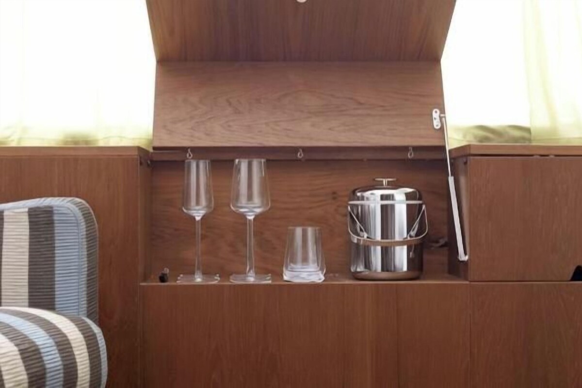 A wooden cabinet with three glasses and a kettle.