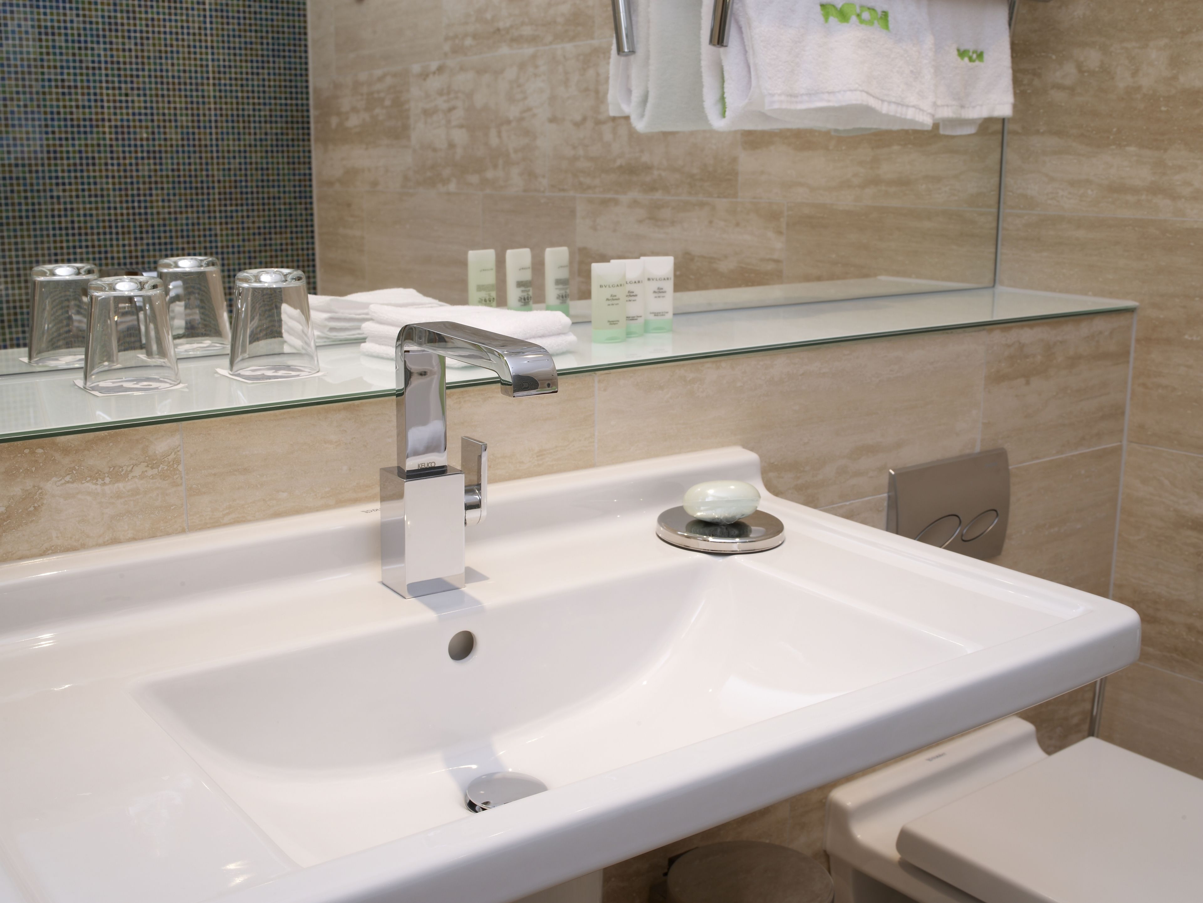 A modern bathroom with a white sink, a glass shelf above it, and a mirror reflecting the room.
