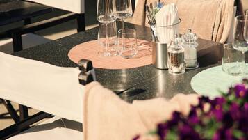 A dining table set with glassware and a placemat, surrounded by chairs with white cushions.