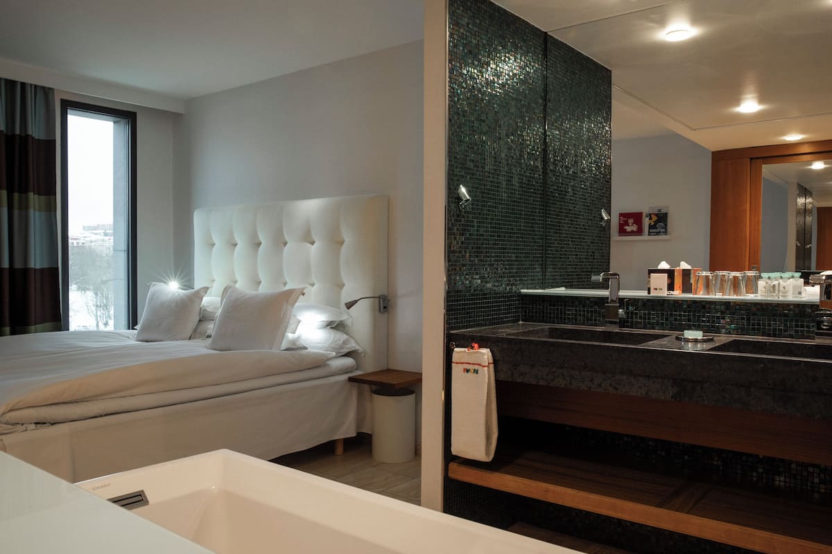 Ett modernt hotellrum med en stor säng, ett separat badrum med en stor spegel och utsikt över staden.