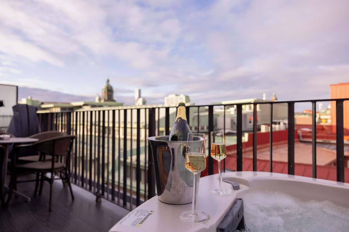 En balkong med ett bord där en champagneflaska och två glas står, med utsikt över en stadsbild med byggnader och en kupolformad konstruktion.