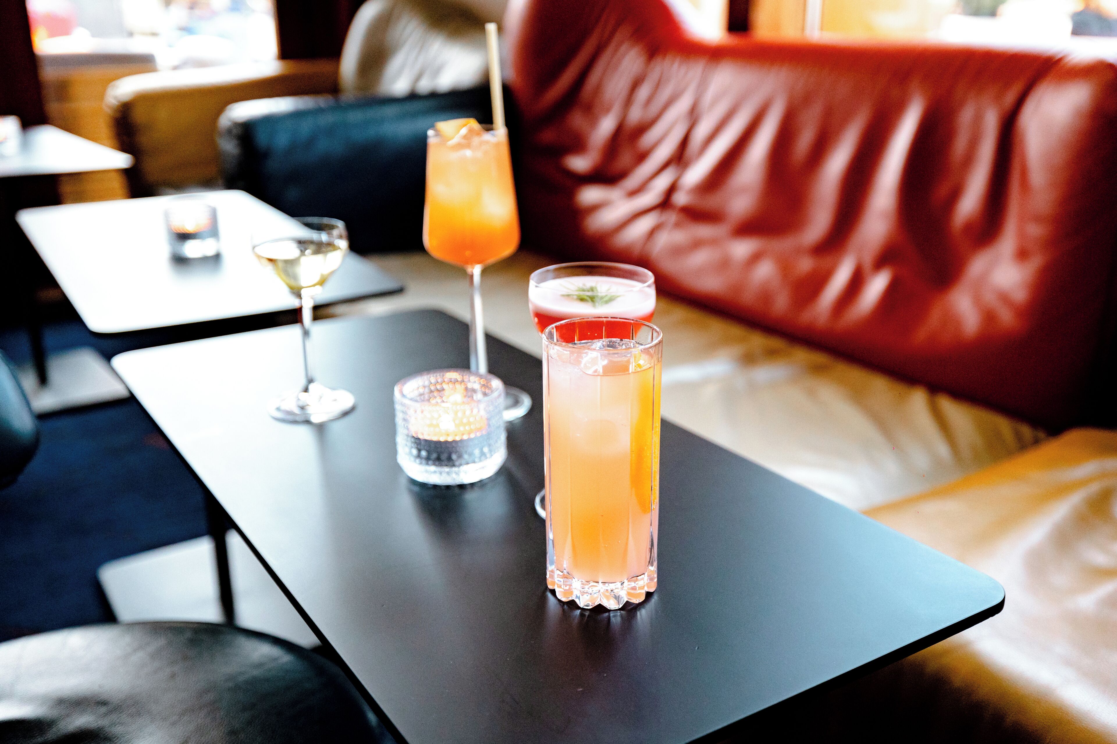 En bar med to cocktails på et bord, et stearinlys og en lædersofa i baggrunden.