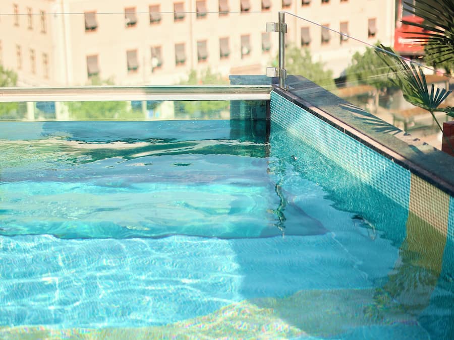 A swimming pool with clear water, a tiled edge, and a building with multiple windows in the background.