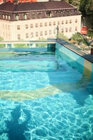 Una piscina con agua cristalina, borde de azulejos y un edificio con múltiples ventanas al fondo.