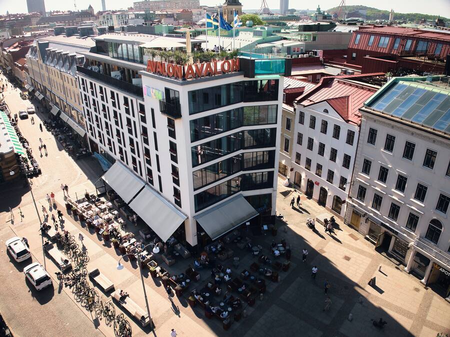 Un hotel de varios pisos con balcones, mobiliario exterior y una terraza en la azotea.