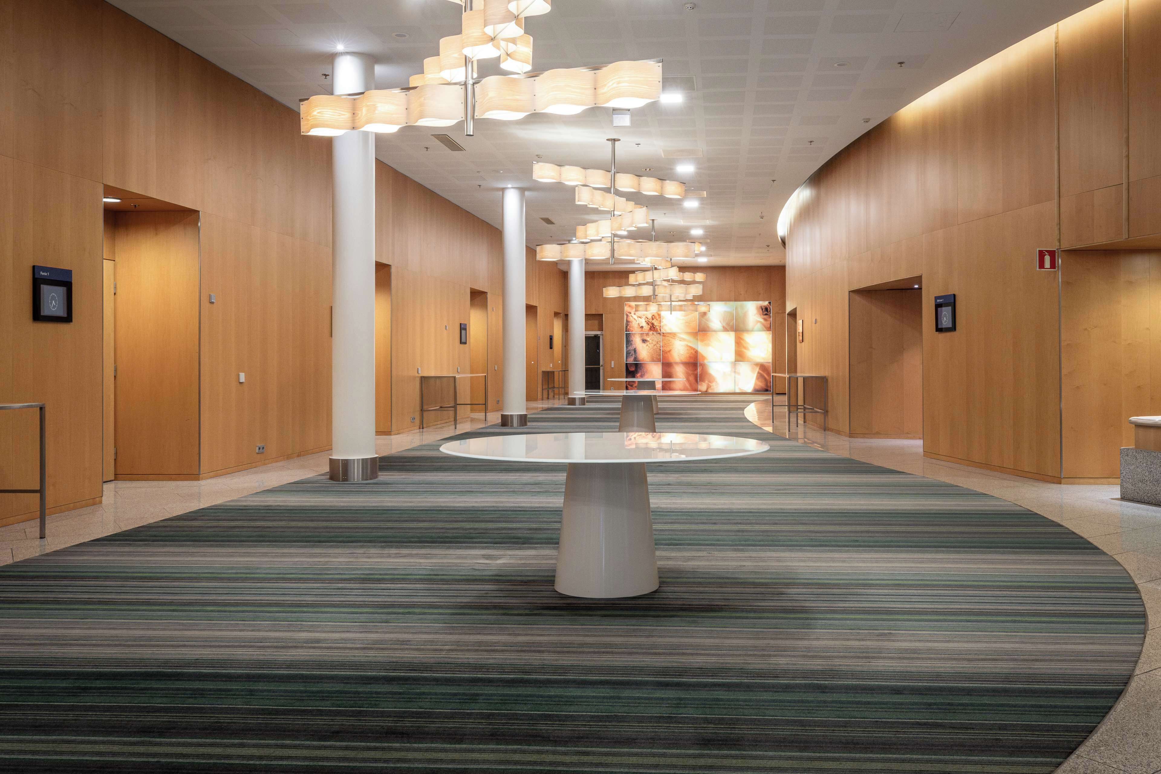Un hall espacioso con una mesa redonda central, paneles de madera y una alfombra estampada.