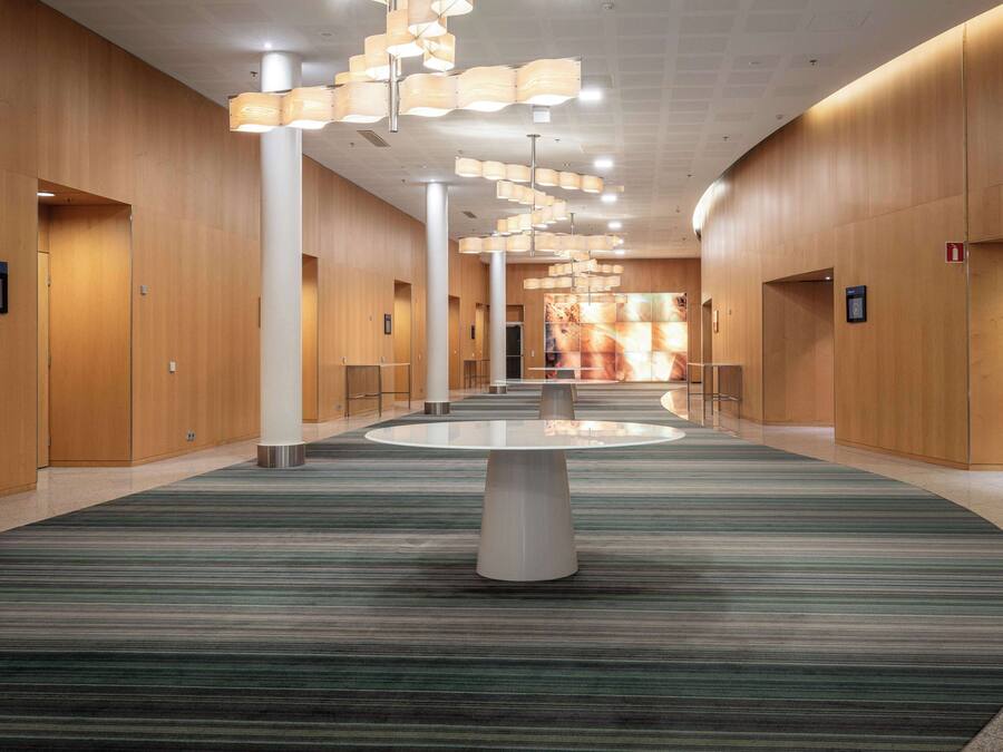 Un hall espacioso con una mesa redonda central, paneles de madera y una alfombra estampada.