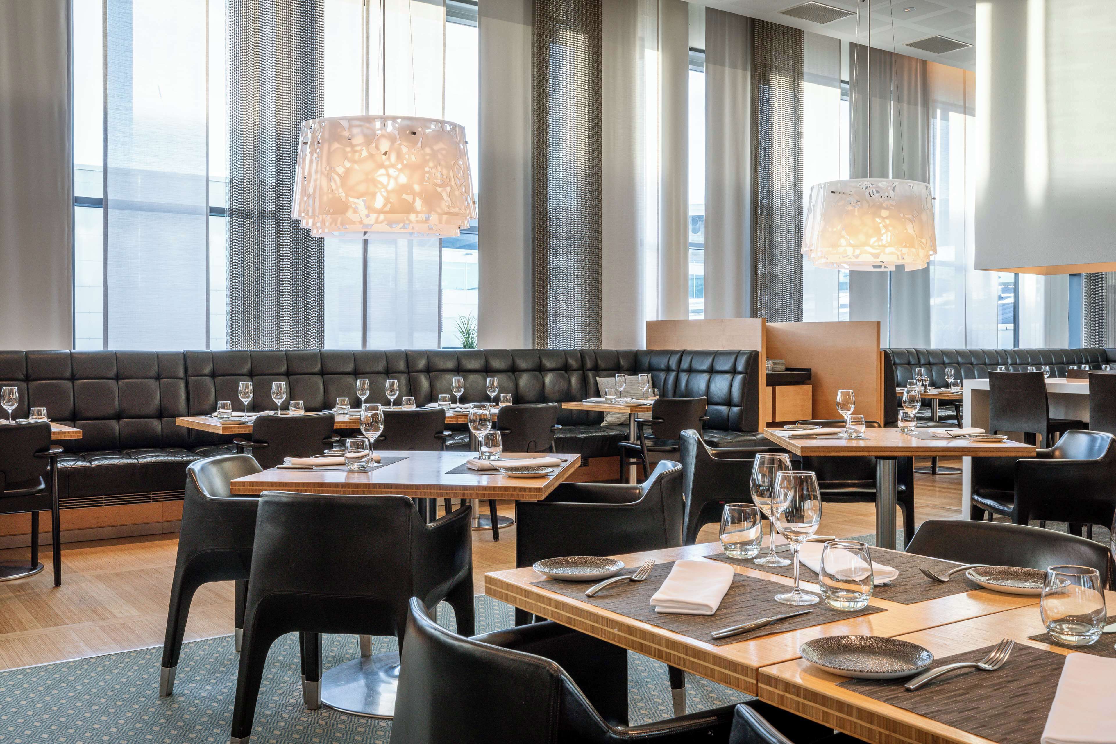 Un ristorante moderno con sedute in pelle, tavoli in legno e lampade a sospensione.