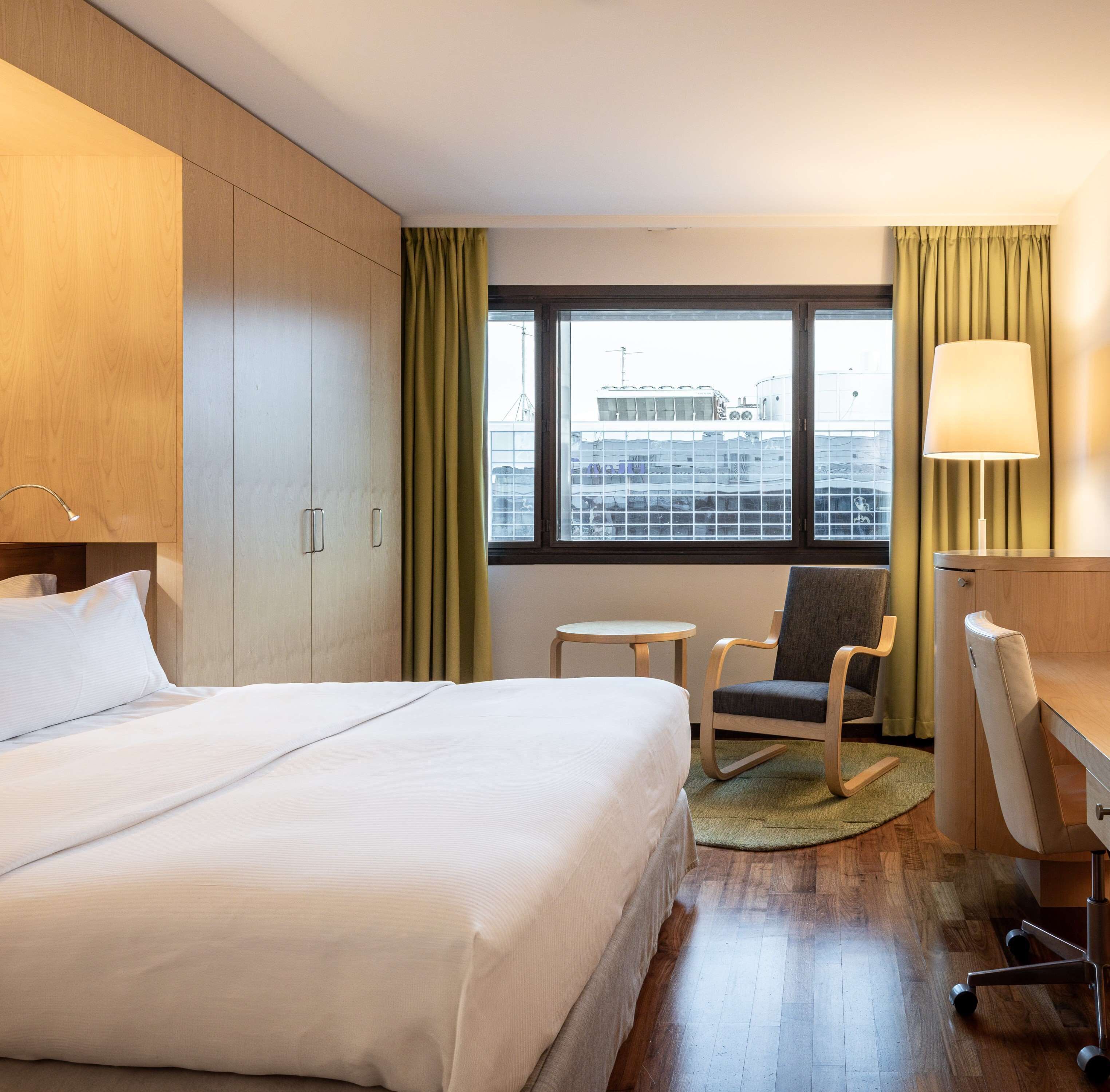 Una habitación de hotel con una cama, un escritorio, una silla, una mesita y una ventana con cortinas.