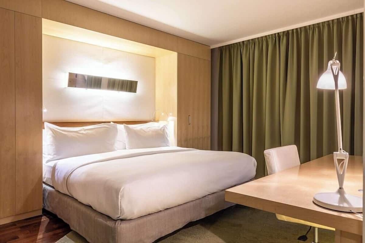 Ein Hotelzimmer mit Bett, Schreibtisch, Lampe und Vorhang.